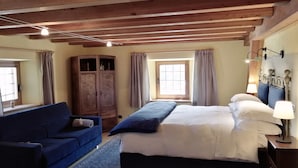A bedroom with a bed, a blue sofa, a wardrobe, and a window with curtains.