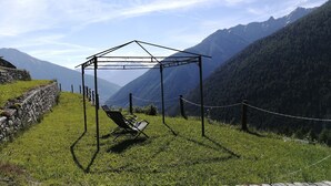 A gazebo with a single chair in a mountainous area, surrounded by stone walls and a chain-link fence.