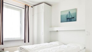 A bedroom with two beds, a window with curtains, a radiator, and a wall-mounted shelf with a sailboat painting. - Bungalow With Sauna & Nature (Earnewald)