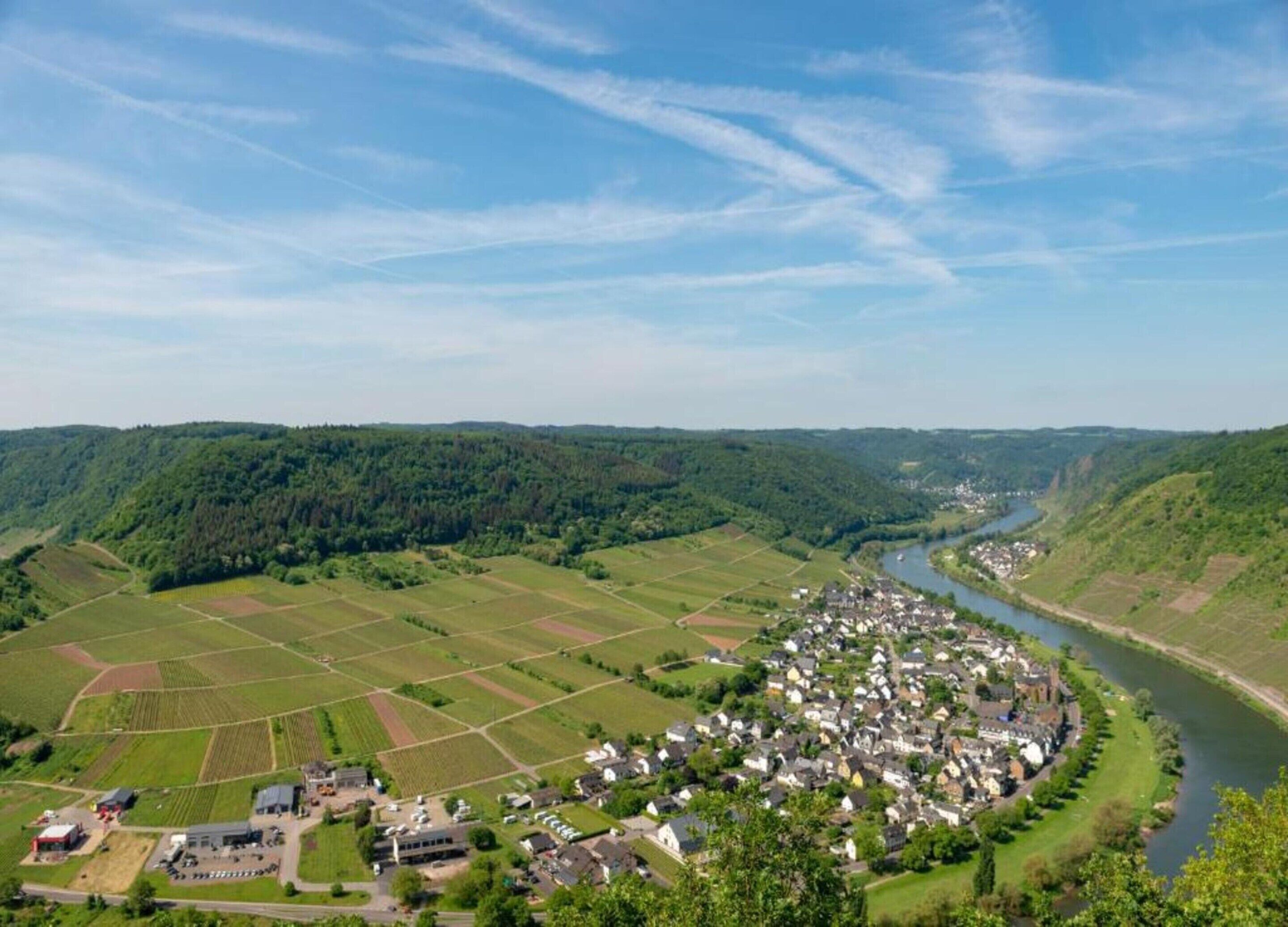 A rural village with a river, surrounded by fields and forested hills.