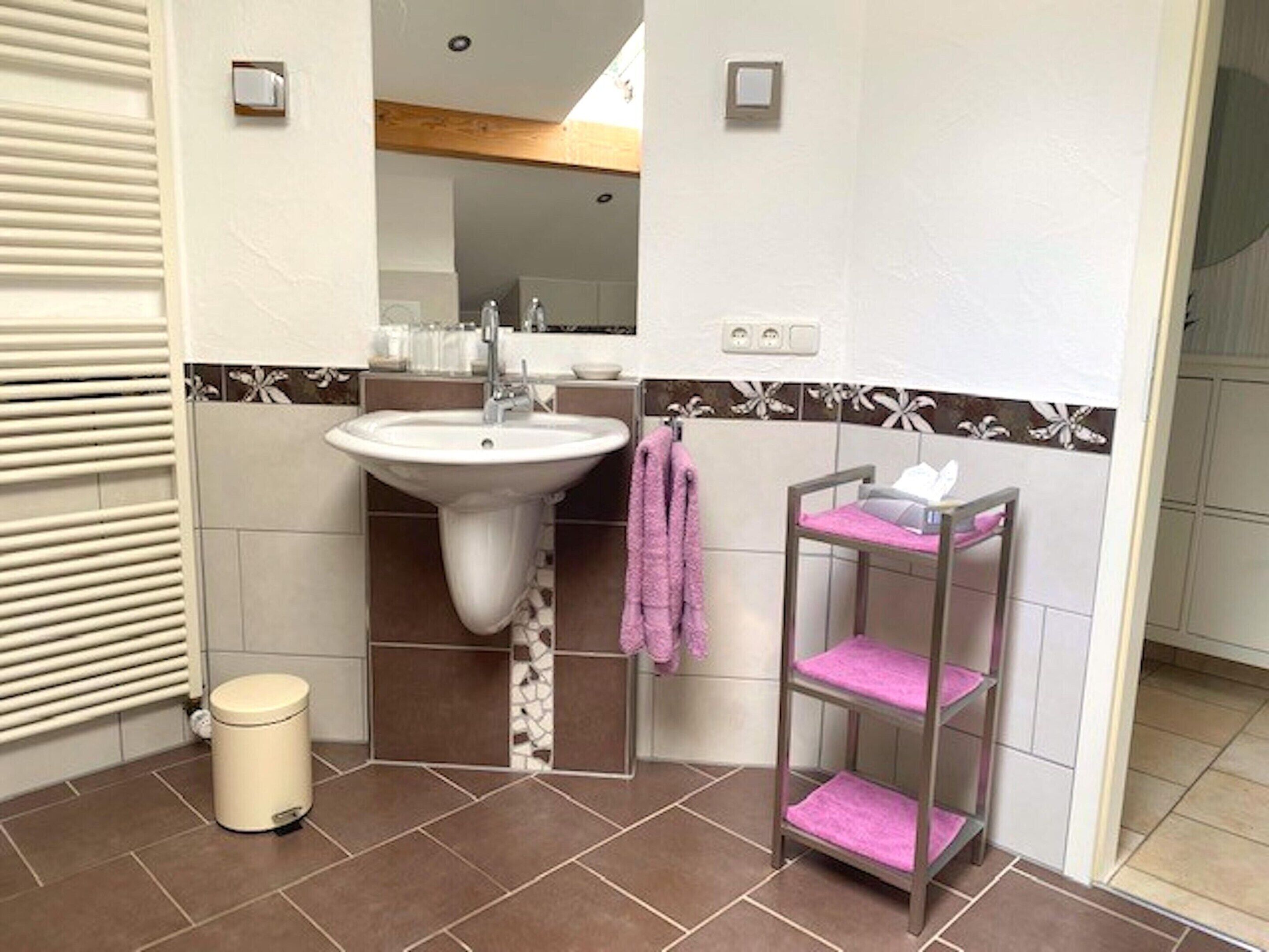 Un baño con lavamanos, espejo, toallero y estante con artículos de tocador.