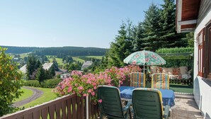 Uma varanda com vista para uma paisagem verde, uma mesa com cadeiras e um guarda-sol floral.