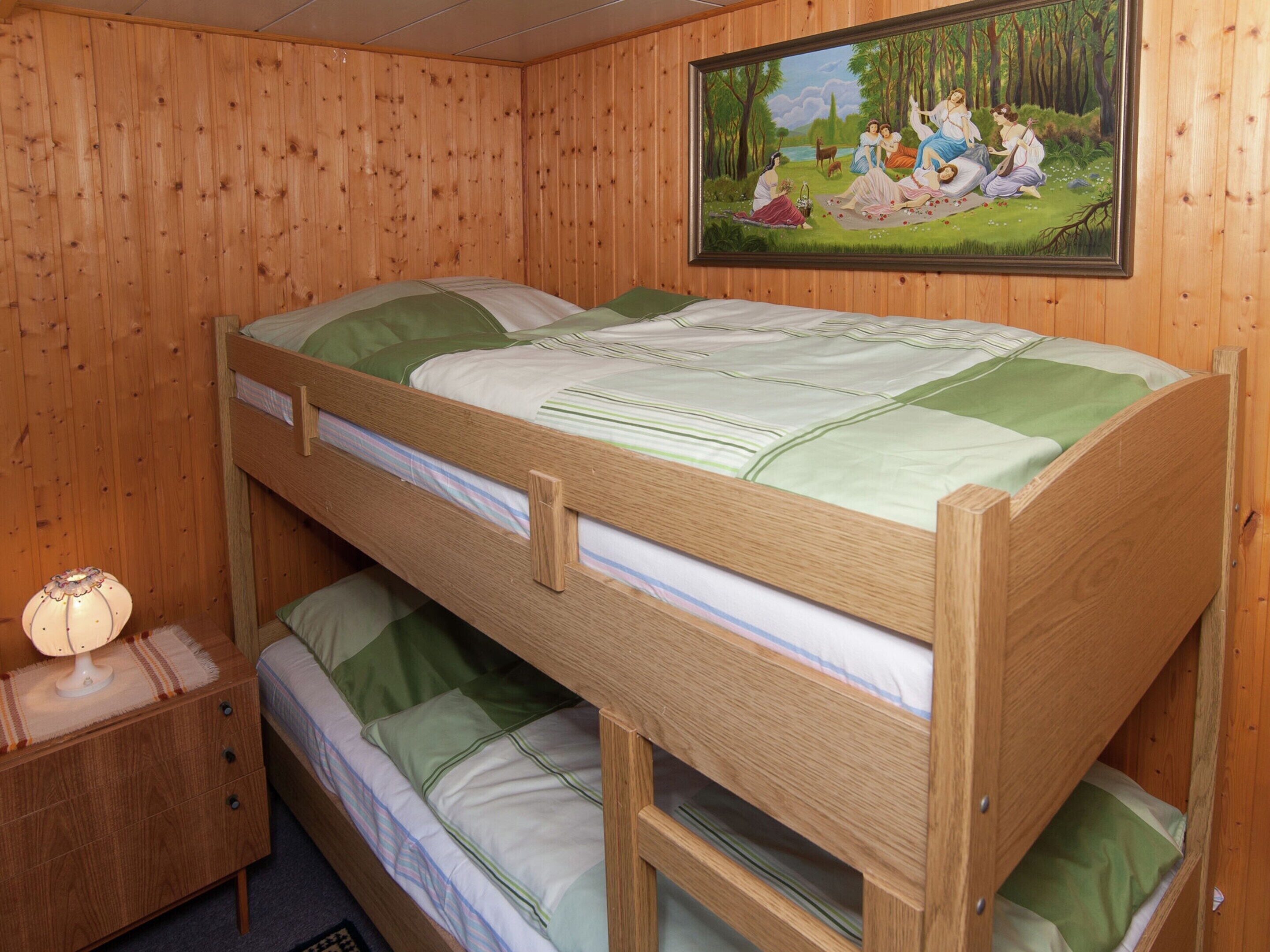 Habitación con literas, paredes de madera, un cuadro en la pared y una mesita de noche con lámpara.