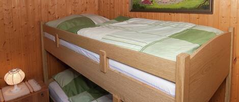 Habitación con literas, paredes de madera, un cuadro en la pared y una mesita de noche con lámpara.