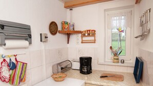 Uma cozinha com fogão branco, cafeteira, torradeira e janela com vista para o verde.