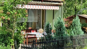 A cozy outdoor seating area with a wooden table and chairs, surrounded by a wooden fence and lush greenery. - Delightful Apartment in Goslar With Garden and Terrace (Goslar)