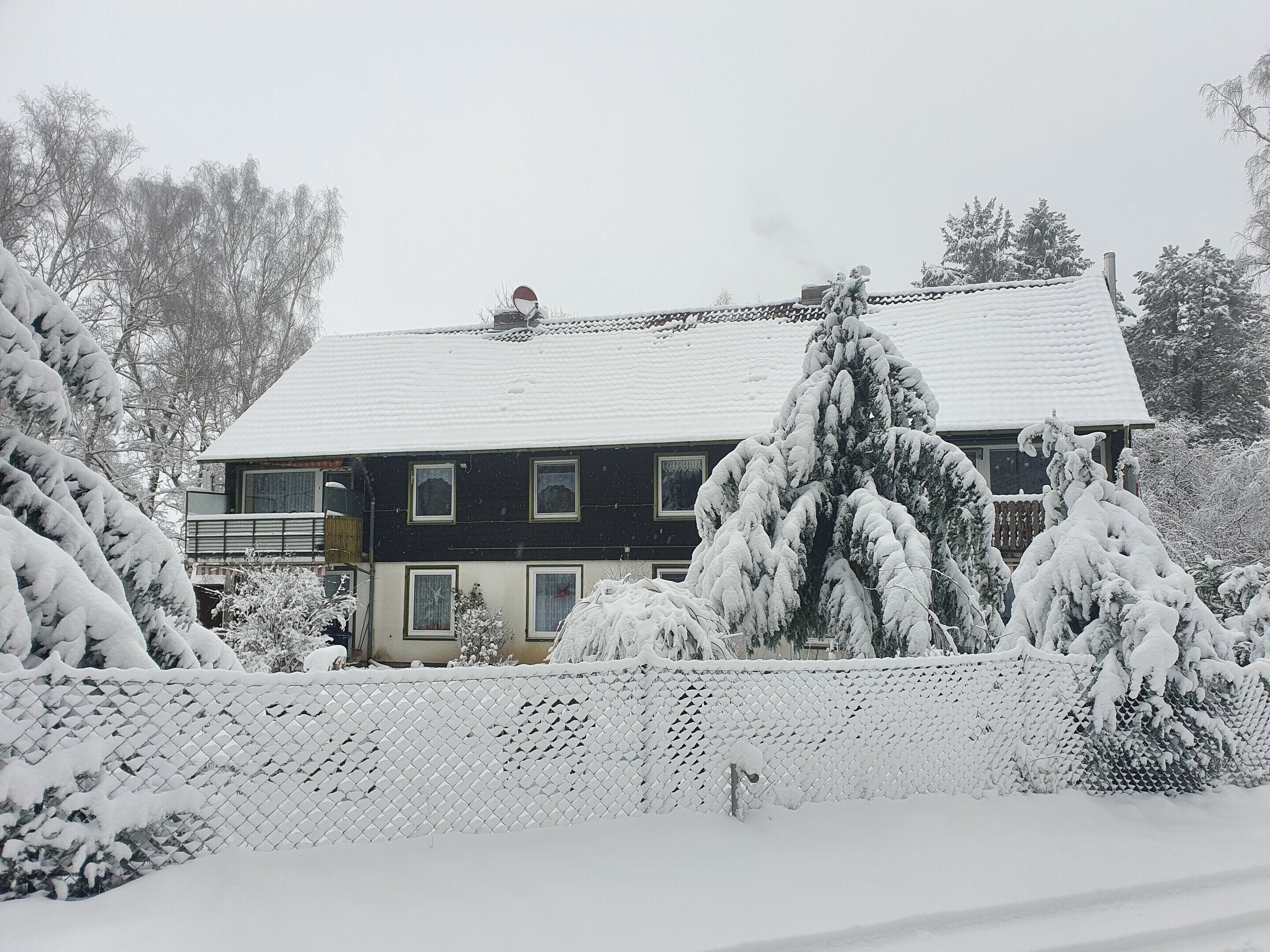 Une maison à deux étages, dont le toit est recouvert de neige, entourée d’arbres.