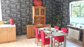 A dining area with a table set for four, red chairs, a wooden cabinet, and a window with a view of trees. - Delightful Apartment in Goslar With Garden and Terrace (Goslar)