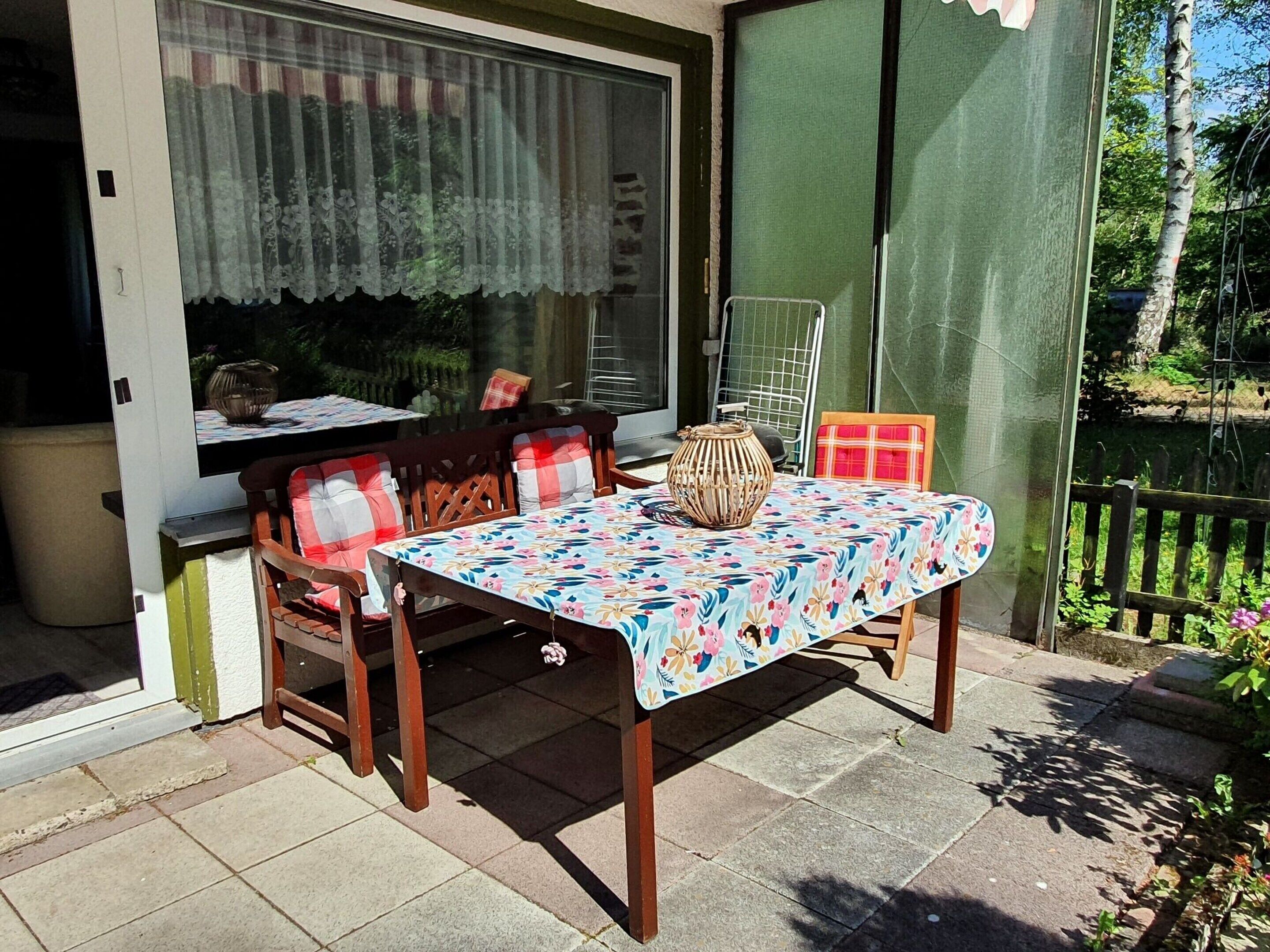 Un patio con una mesa y sillas, una ventana con cortinas y vistas a zonas verdes.