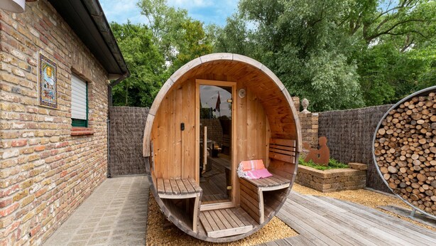 Een houten sauna met een bankje binnen, een deur en een klein bankje buiten.