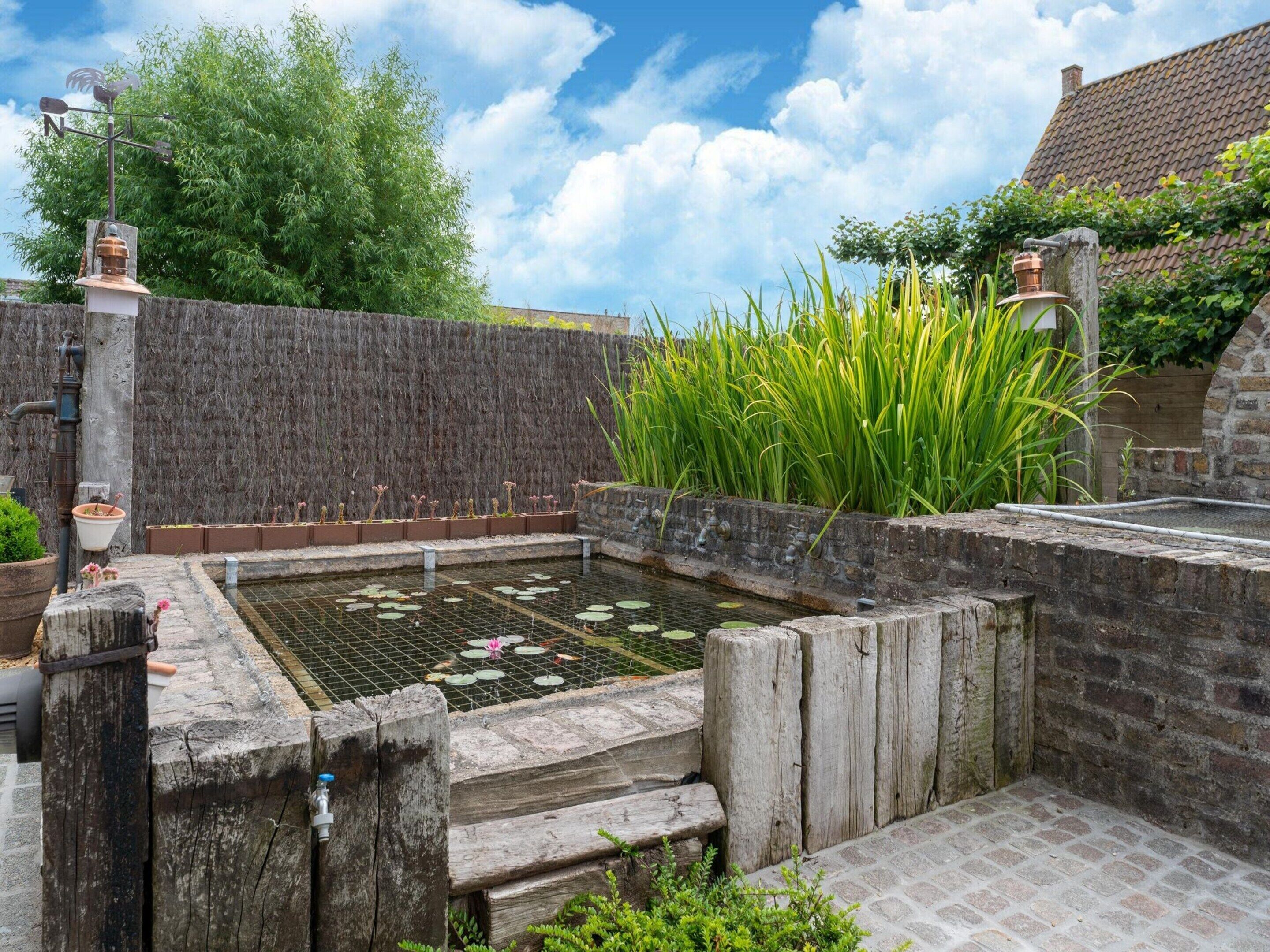 A garden with a pond, wooden steps, and a brick wall.