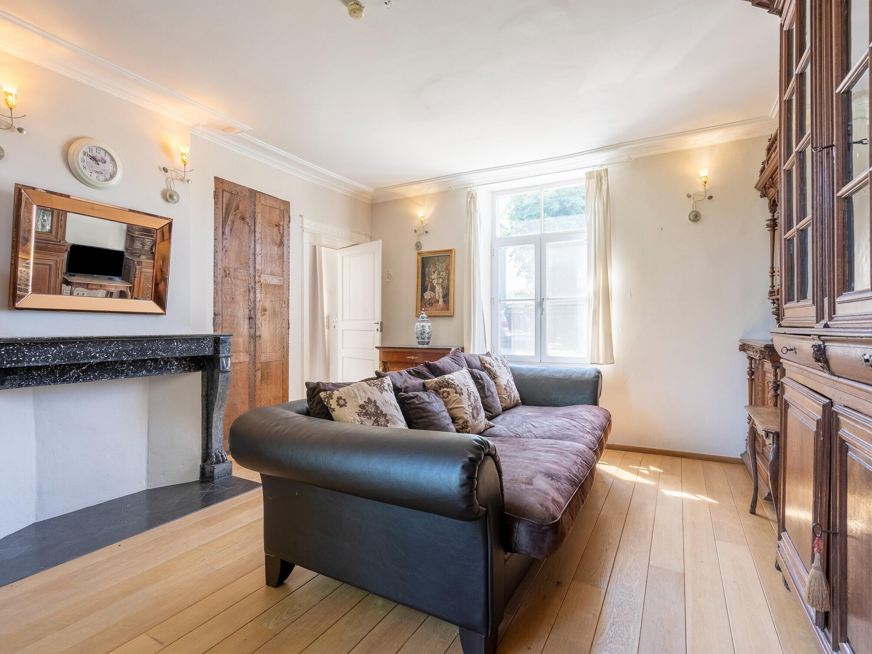 A room with a dark leather sofa, a wooden cabinet, a fireplace, and a large window with curtains.