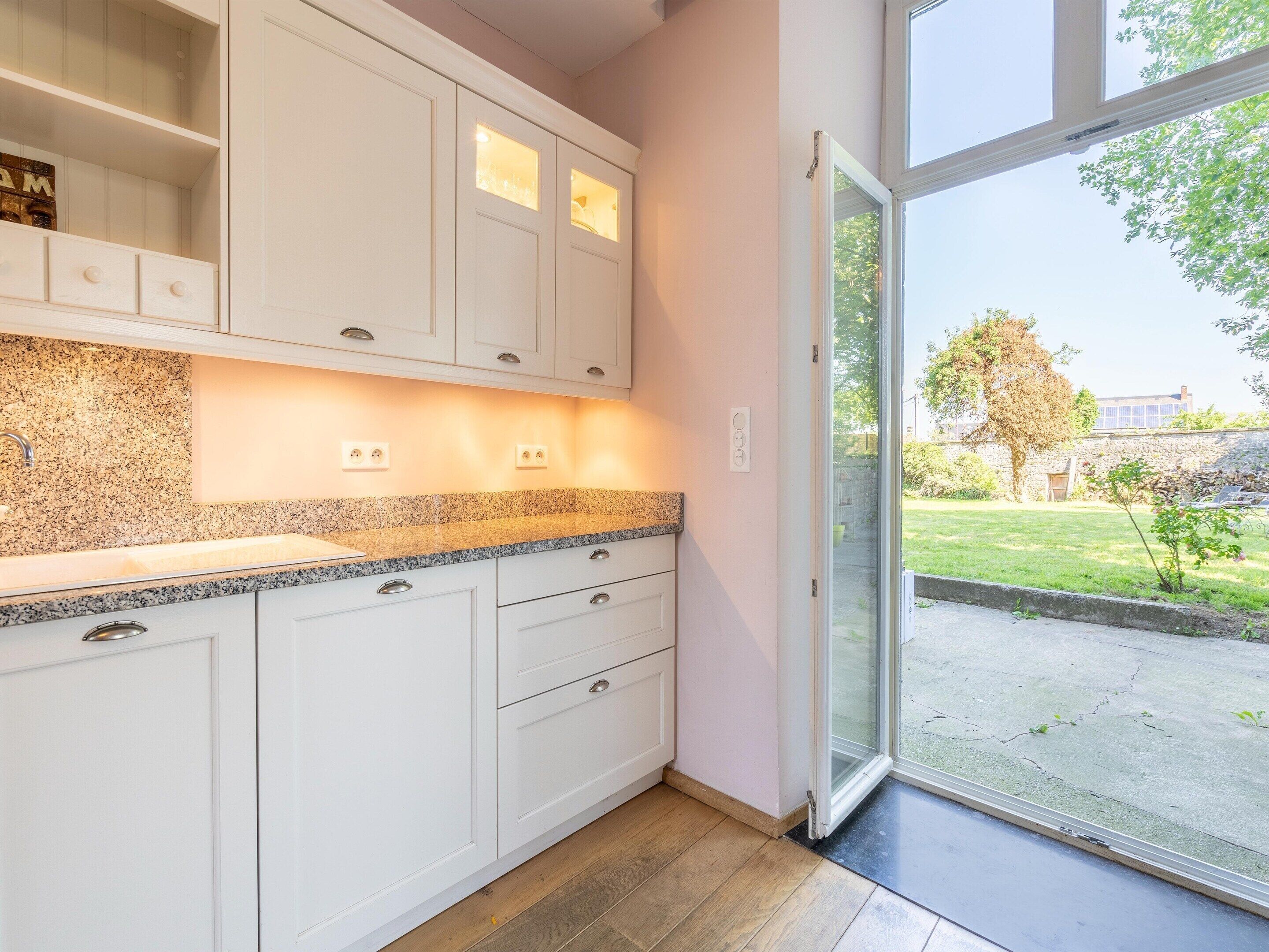 A modern kitchen with white cabinetry, granite countertops, and a view through a glass door to a garden.