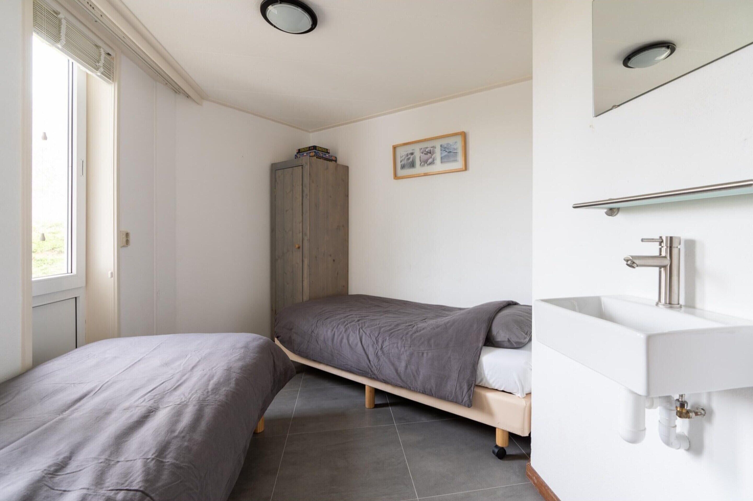A bedroom with a bed, a wardrobe, a bathroom with a sink, and a window.