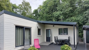 A modern single-story house with a patio area featuring a table and chairs, a sliding glass door, and a small garden with bushes. - Cosy Holiday Home in Appelscha With Garden (Appelscha)