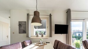 A modern dining area with a long table, brown leather chairs, a hanging pendant light, a flat-screen TV, and a window with curtains. - Cosy Holiday Home in Appelscha With Garden (Appelscha)