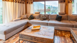 A modern living room with a large L-shaped sectional sofa, a rustic coffee table, and large windows with curtains. - Home in Heart of Belgian Nature (Vresse-sur-Semois)