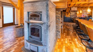 A stone-built fireplace with a wooden ceiling and a dining area with a long table and chairs. - Home in Heart of Belgian Nature (Vresse-sur-Semois)