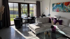 A modern living room with a glass coffee table, a sofa, a dining table with chairs, and a large window with curtains. - Holiday Home in Gonnersdorf With Sauna (Gonnersdorf)