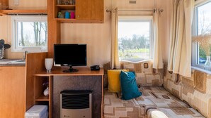 A compact RV interior with a kitchenette, a flat-screen TV, a heater, and a window with curtains. - Nice Holiday Home in Appelscha With Garden (Appelscha)