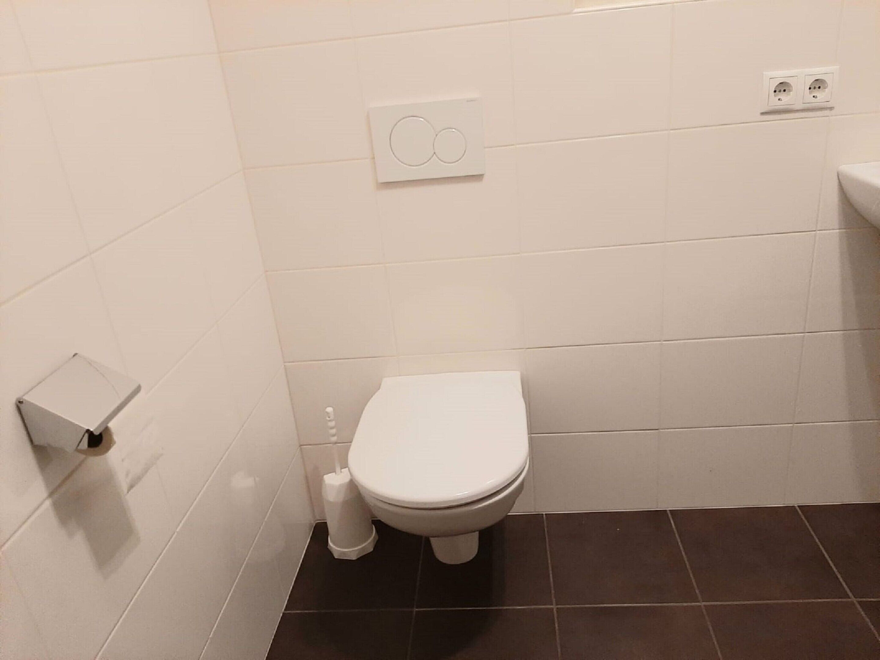 Un baño pequeño y limpio con azulejos blancos, un inodoro, un bidé y un lavamanos.