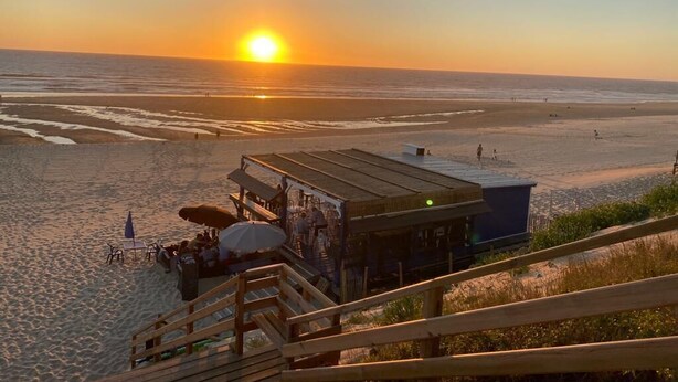 A beachside view with a sunset, a wooden deck, and a small building with outdoor seating.
