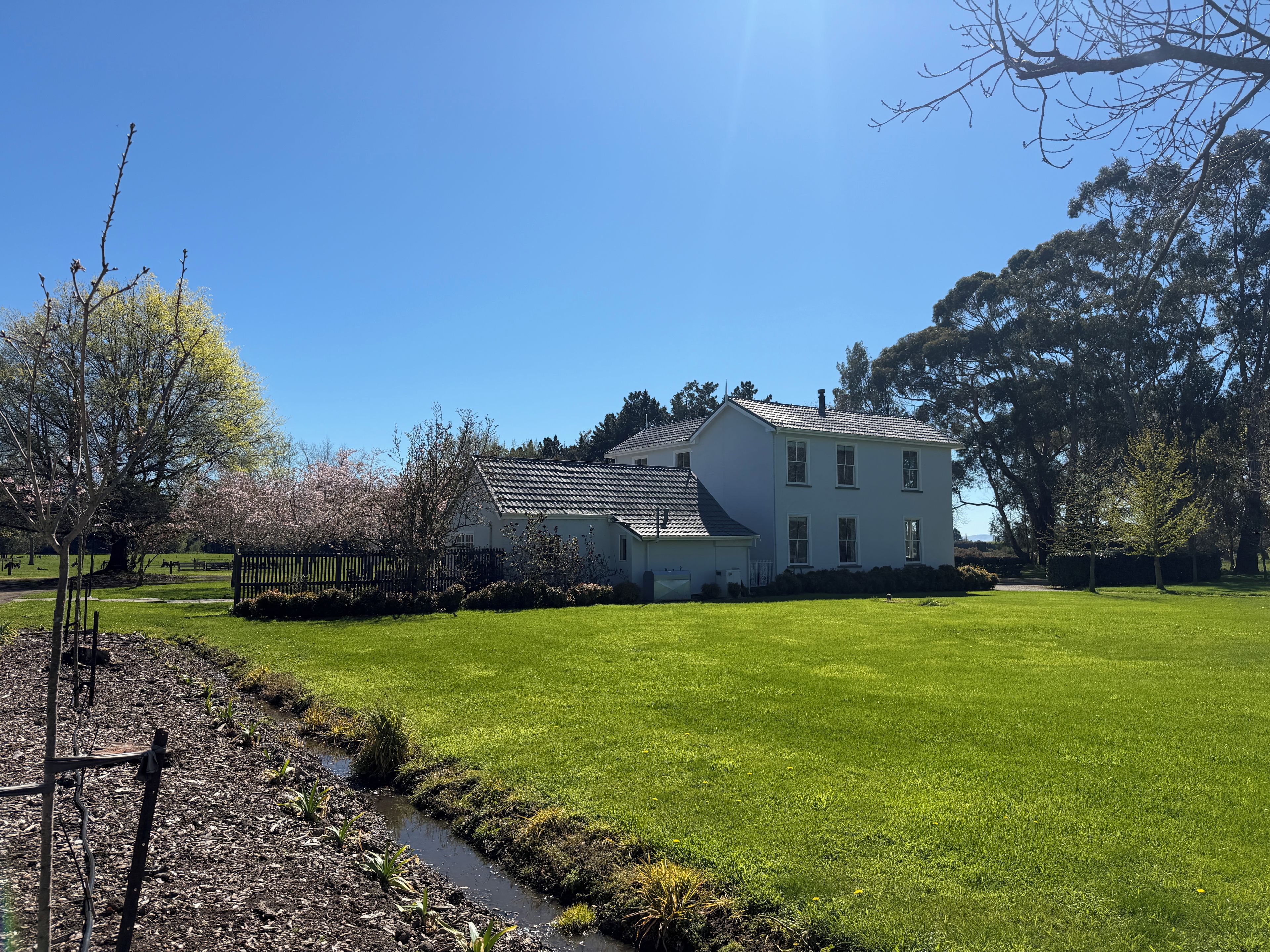A two-story house with a sloped roof, surrounded by a well-maintained lawn and a small stream.