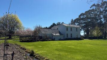 A two-story house with a sloped roof, surrounded by a well-maintained lawn and a small stream.