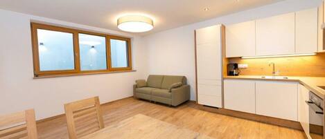 A modern, compact living space with a dining area, a sofa, a kitchenette, and a large window.
