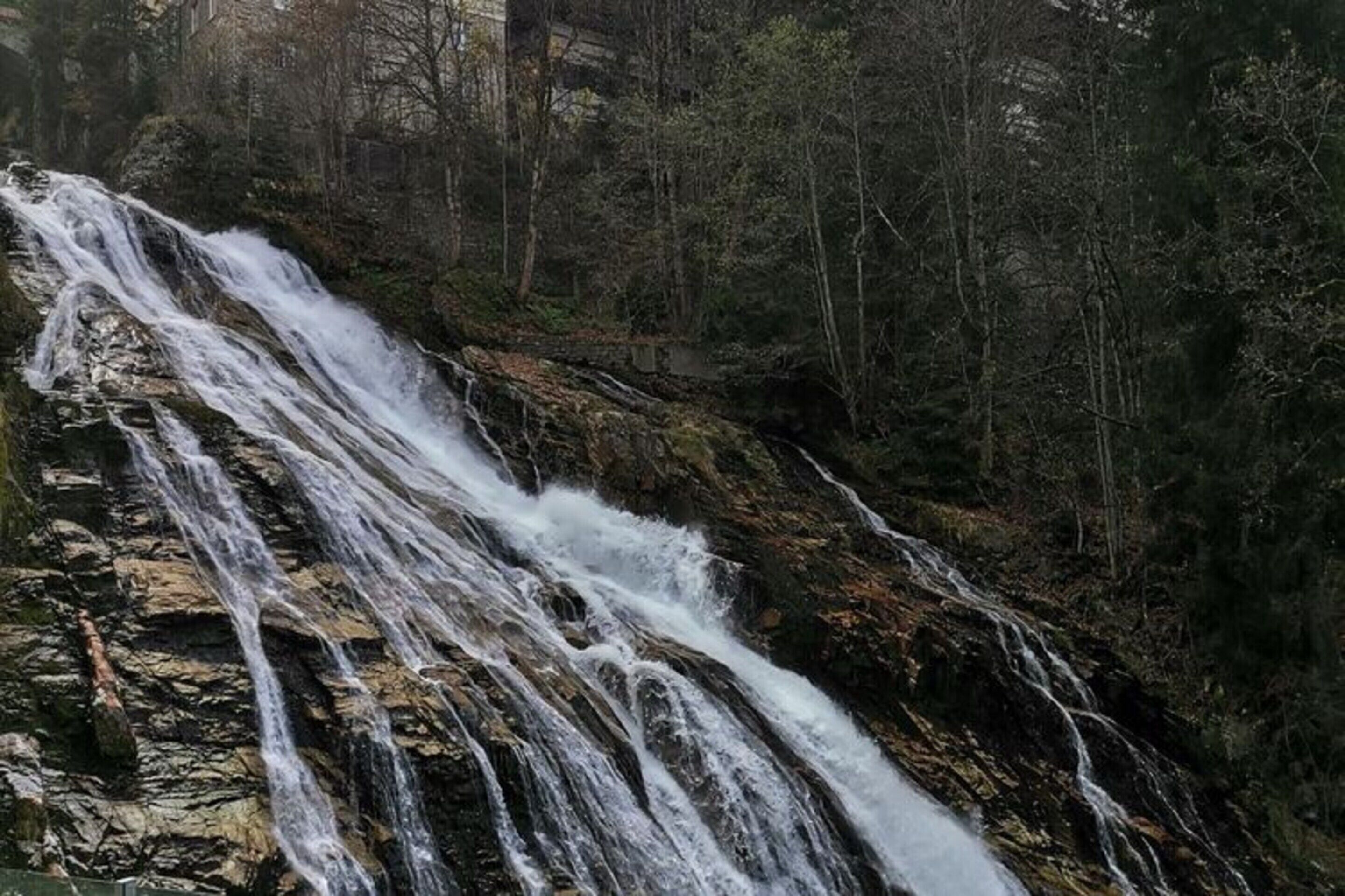 Een waterval die over rotsachtig terrein stroomt, omgeven door dicht bos.