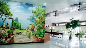 A conference room with a mural of a coastal landscape, a ceiling fan, and potted plants. - WINER HOTEL PALEMBANG (Palembang)
