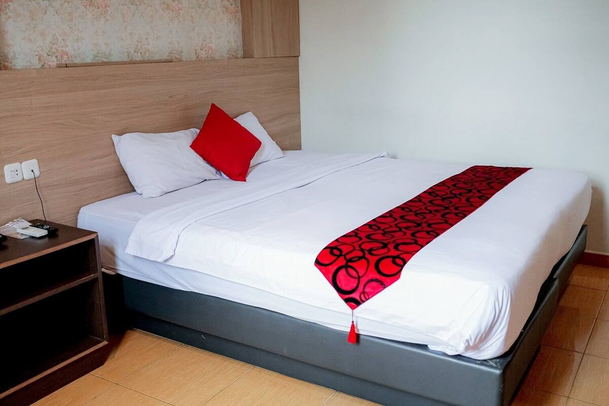 Cama bem arrumada com roupa de cama branca e manta com padrão preto e vermelho.