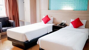 A hotel room with two beds, each with white bedding and red pillows, a bedside table with a phone, and a view of a blue textured wall. - WINER HOTEL PALEMBANG (Palembang)