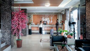A hotel reception area with a marble reception desk, a receptionist, a guest with luggage, and a seating area with a coffee table and chairs. - WINER HOTEL PALEMBANG (Palembang)