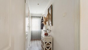 A narrow hallway with a wooden floor, a white console table with decorative items, and a mirror on the wall.