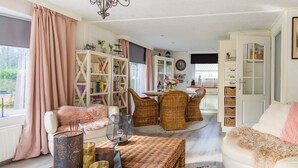 A cozy living room with a white sofa, wicker chairs, a bookshelf, and a dining area with a table and chairs.