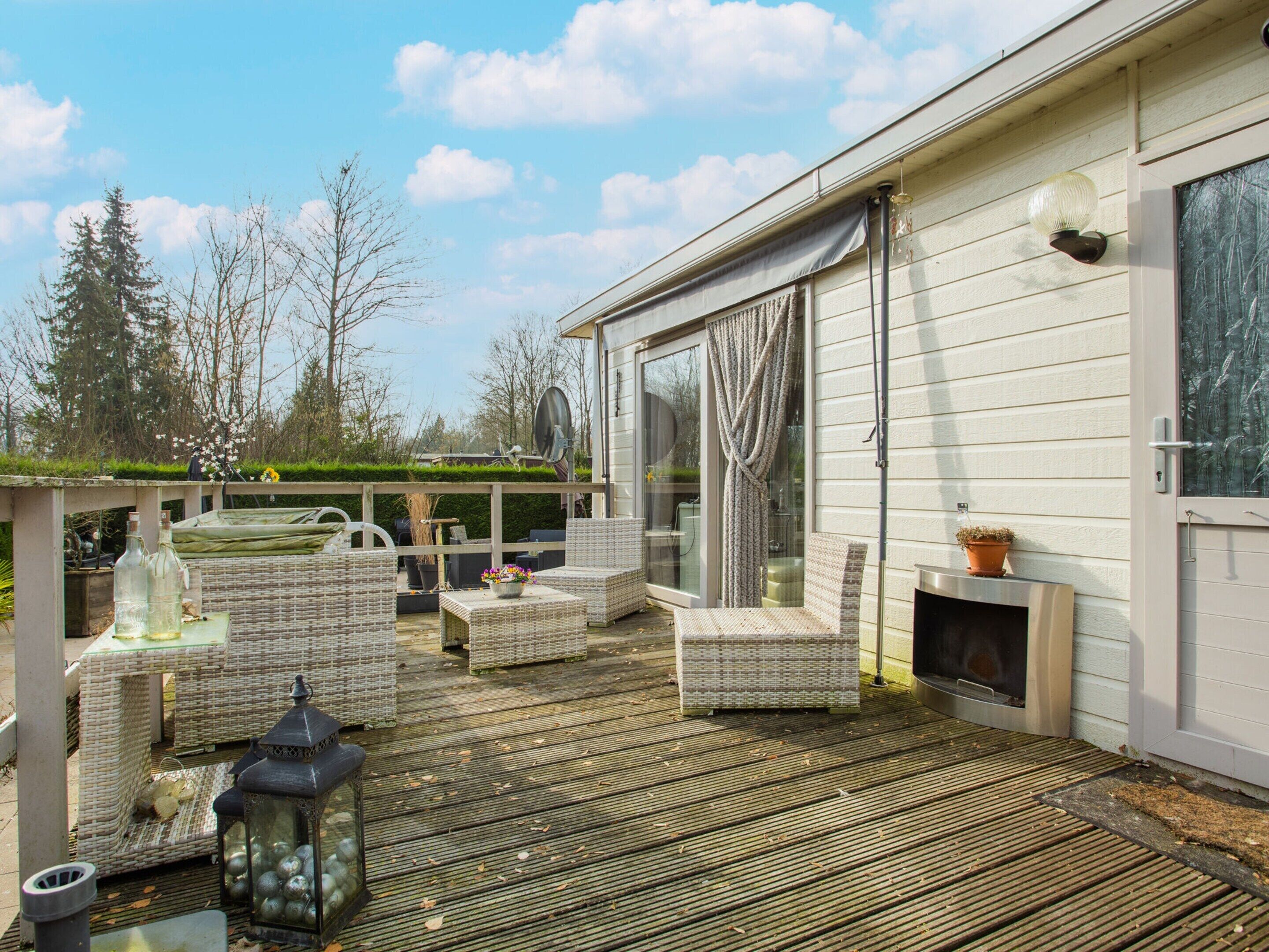 A wooden deck with wicker furniture, a glass bottle, and a lantern.