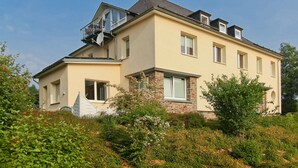 A two-story house with a balcony on the upper floor, a satellite dish, and a stone base. - Ferienwohnung im Sauerland (Erndtebrück)