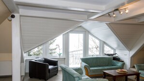 A spacious attic room with a sloped ceiling, large windows, and a mix of seating including a black leather sofa and two light blue armchairs. - Ferienwohnung im Sauerland (Erndtebrück)