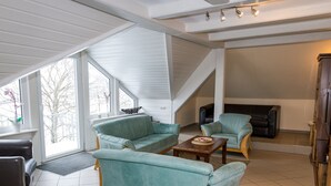 A spacious living room with a high ceiling, large windows, and a fireplace. - Ferienwohnung im Sauerland (Erndtebrück)