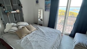 A bedroom with a bed, a small bedside table, a mirror, and a view of the sea through a window. - Villa, golden island view, a stone's throw from the beach. Breathtaking view! (Saint-Raphaël)