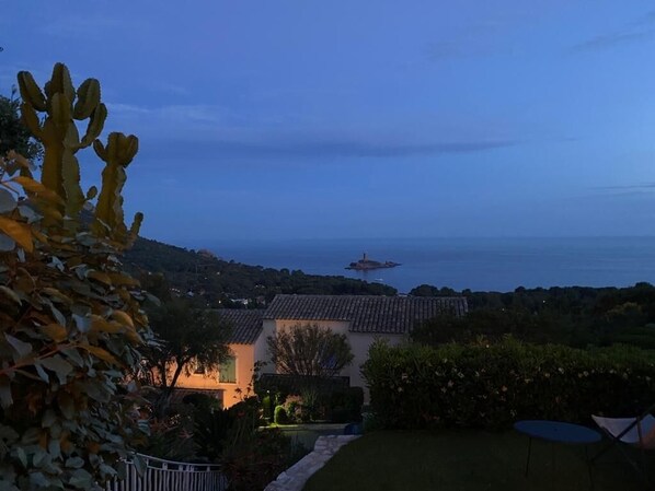 A coastal landscape with a view of the sea, a distant island, and a building with a tiled roof.