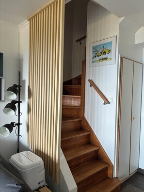 A staircase with wooden steps and a handrail, a white wall with a framed picture, and a white trash bin.