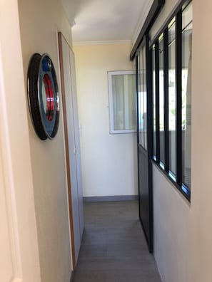 Ein schmaler Flur mit einer Tür links, einem Fenster mit Vorhängen rechts und einem runden Gegenstand an der Wand.