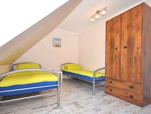 A small, triangular attic bedroom with two metal bunk beds, a wooden wardrobe, and a painting on the wall.