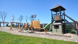 A playground with climbing structures, a slide, and a small building with a flag. - Seaside Cottage With Terrace and Lovely Garden (Darlowo)