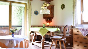 Un comedor acogedor con una mesa y banco de madera, una lámpara colgante y vistas amplias a través de grandes ventanales.