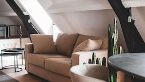 Et hyggeligt loftværelse med en beige sofa, et lille rundt bord og en kaktus.