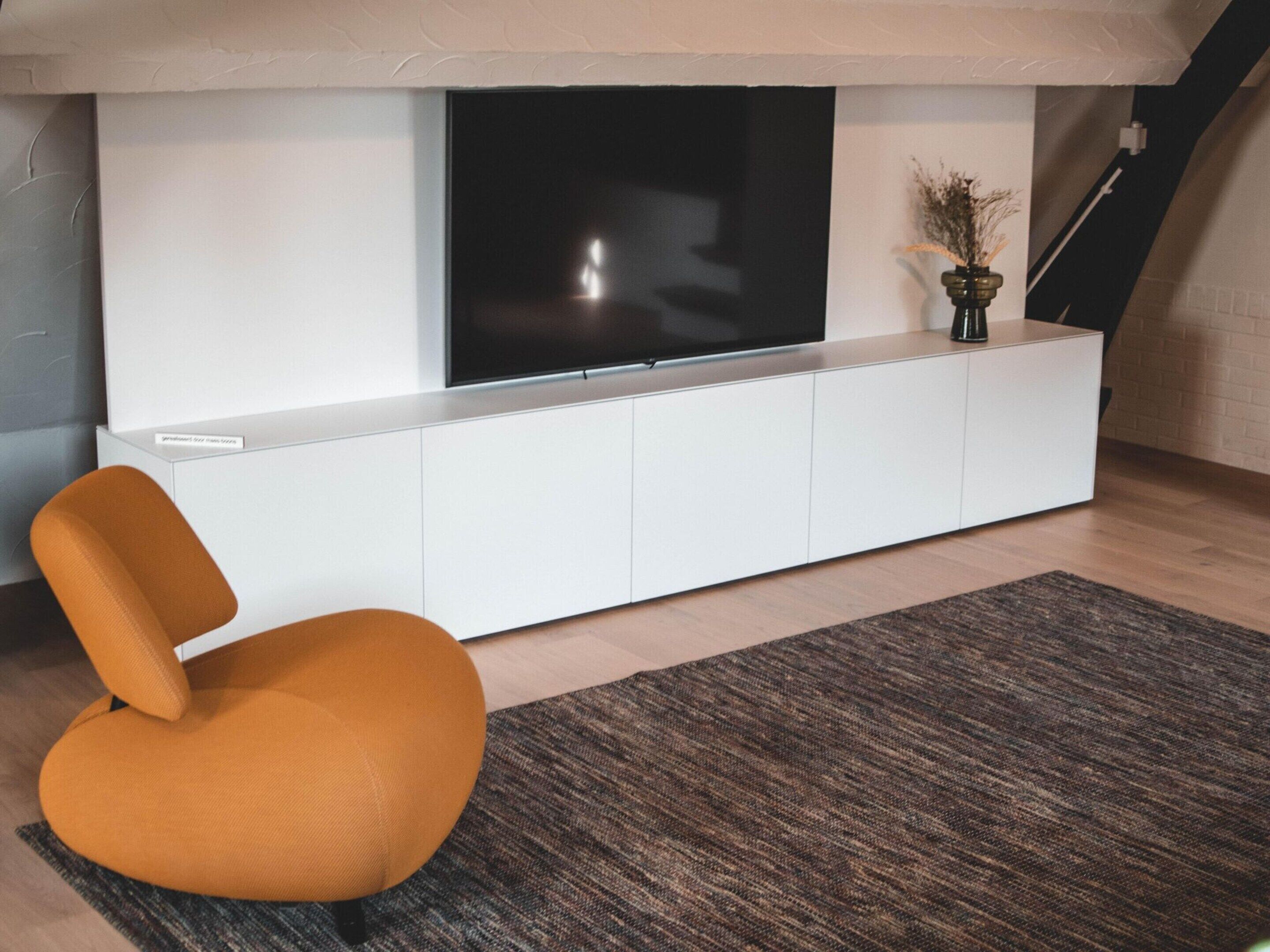 A modern living room with a flat-screen TV mounted on a white cabinet, a mustard-colored chair, and a textured rug on the floor.