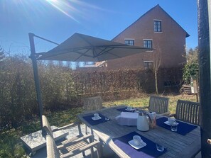 An outdoor patio with a table set for two, a white coffee pot, and a wooden chair. - Holiday Home in Bazel for 6 Person (Kruibeke)